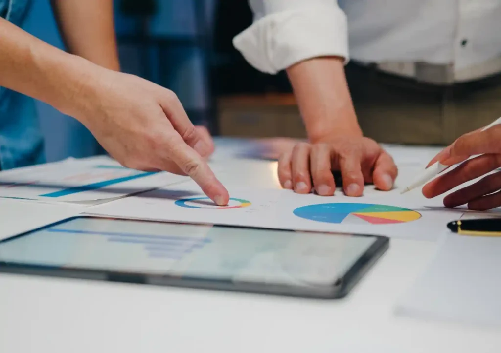 Close-up of colleagues pointing at pie charts and analyzing performance data on a desk to evaluate the results of A/B testing for search ads.
